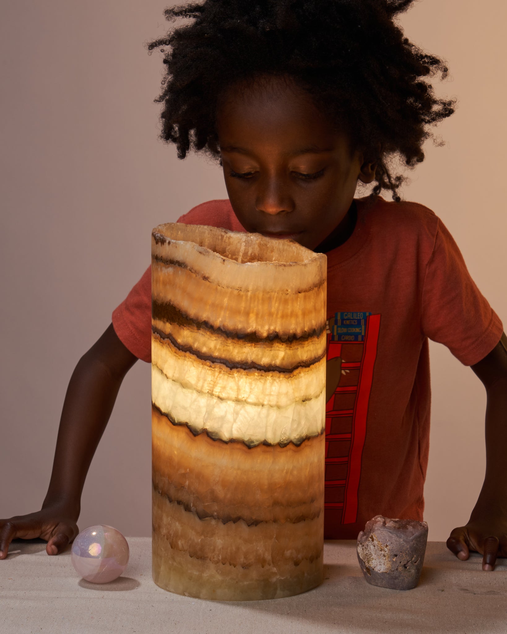 Young boy admiring Mexican Onyx lamp. Mexican Onyx offers protection, strength, and elegance. Perfect for decor and gifting. Included: One polished, cut base Mexican Onyx lamp